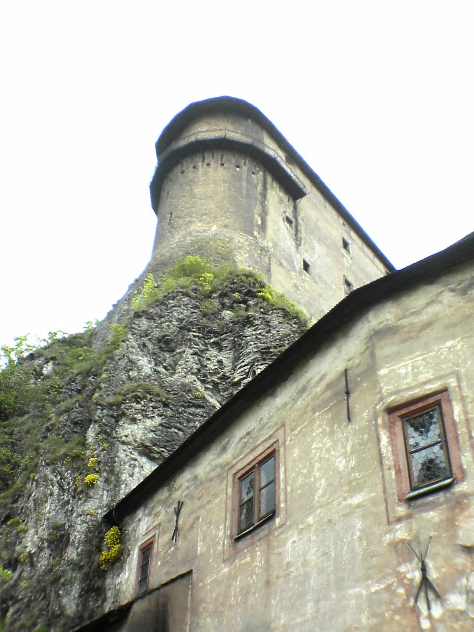 De bovenste burcht van Oravský hrad op een steile rots, met witte muren en rode daken boven de bomen.